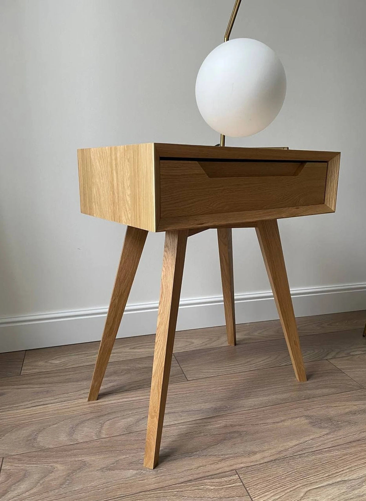 Oak drawer side table with tapered legs and globe lamp styled beside wall