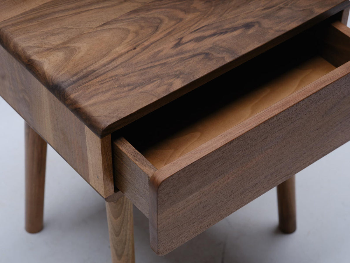 Close-up of walnut nightstand drawer open showing fine wood joinery and grain
