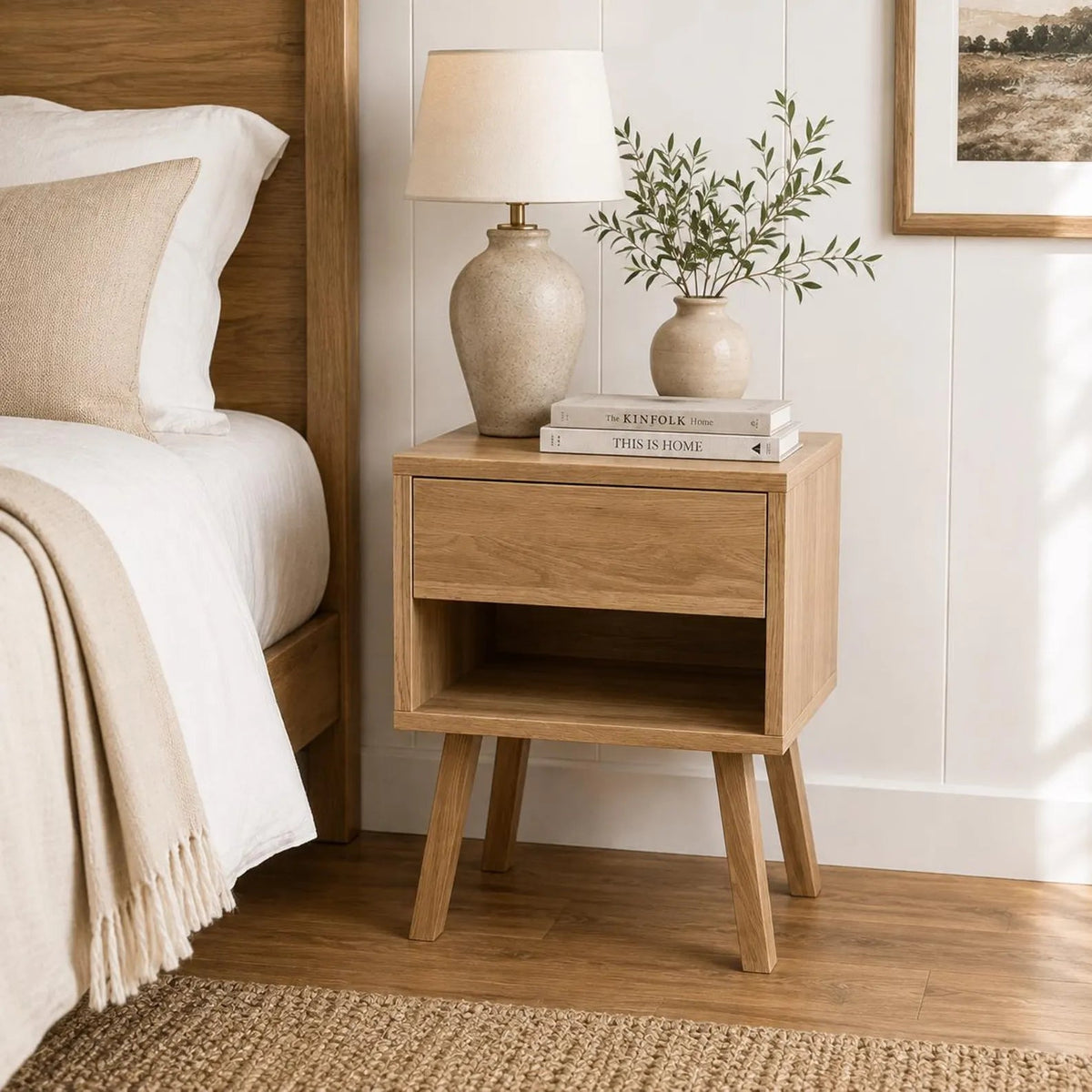 Oak open shelf nightstand with lamp and vase styled beside bed in bright bedroom